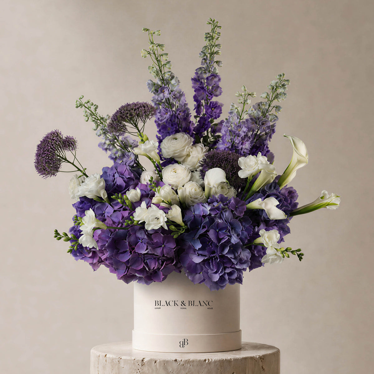 Violet and white arrangement of hydrangea, delphinium, ranunculus and calla lily in a Black & Blanc box
