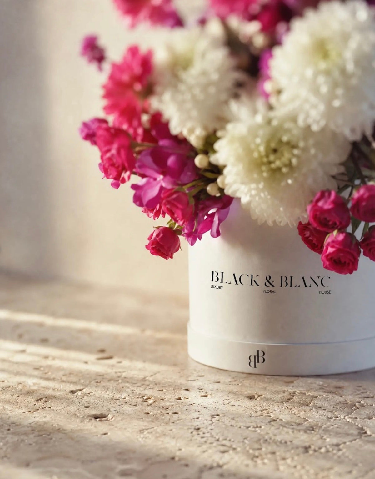 Close detail of pink spray roses and white chrysanthemum against a Black & Blanc box