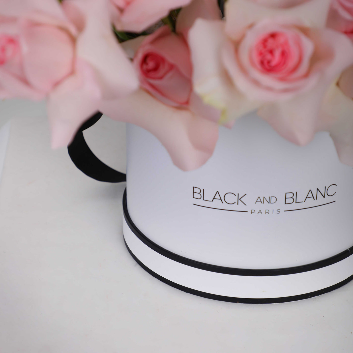 Cylindrical white box with BLACK and BLANC PARIS, topped with fresh pink roses