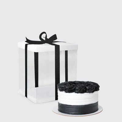 Elegant white gift box with black ribbon next to a round cake with black roses