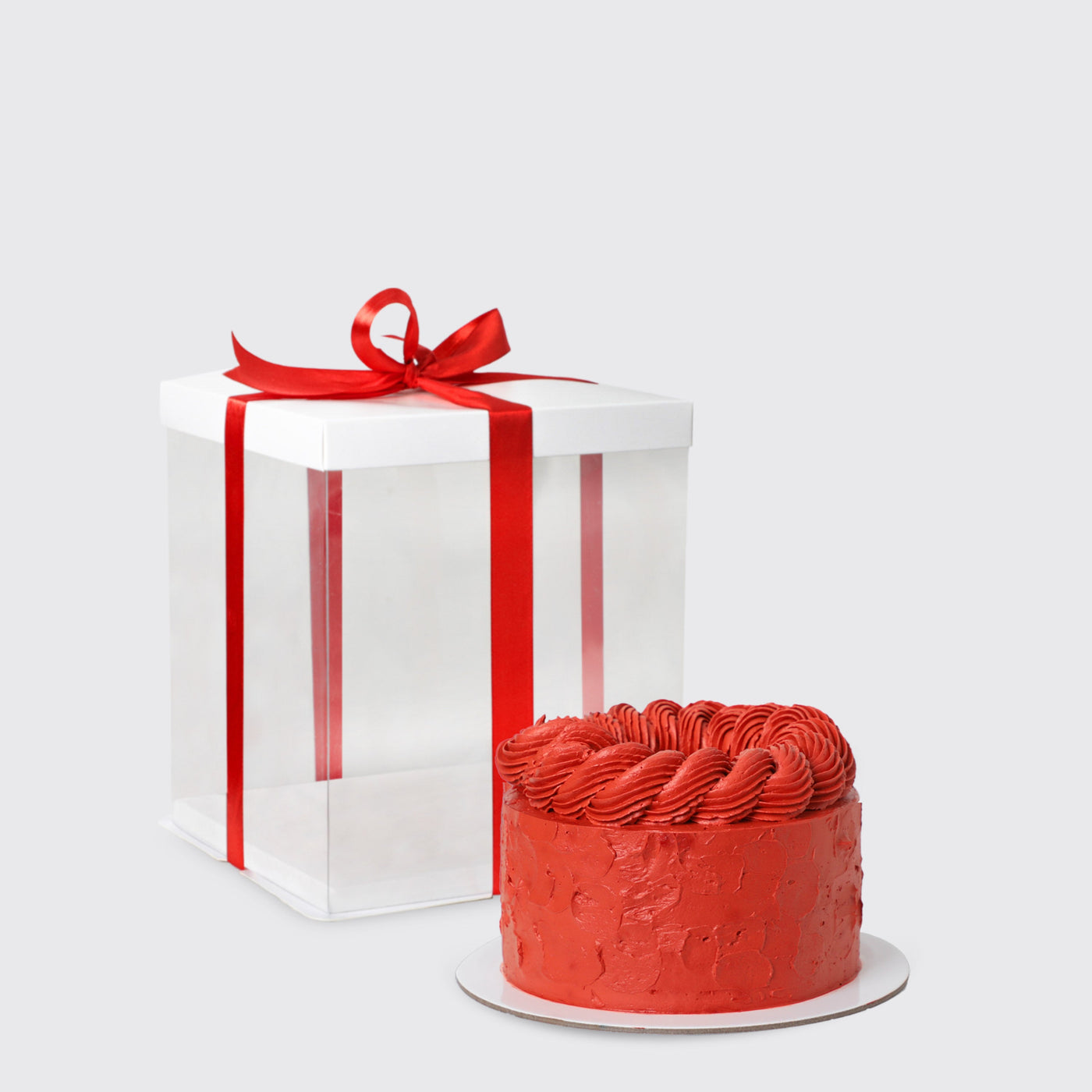 Red-frosted cake with swirls next to a white gift box with a red ribbon from Cartier