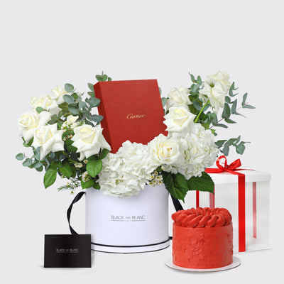 Floral arrangement in white container with Cartier box, red cake, and gift box