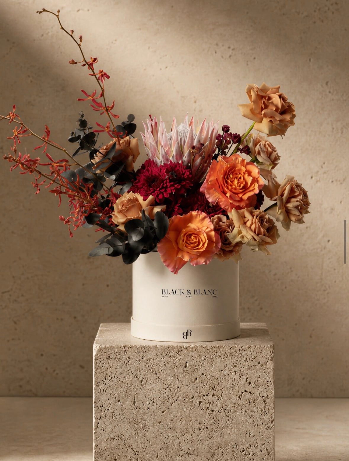 King protea, oxblood chrysanthemum and copper roses in a Black & Blanc box on a travertine plinth