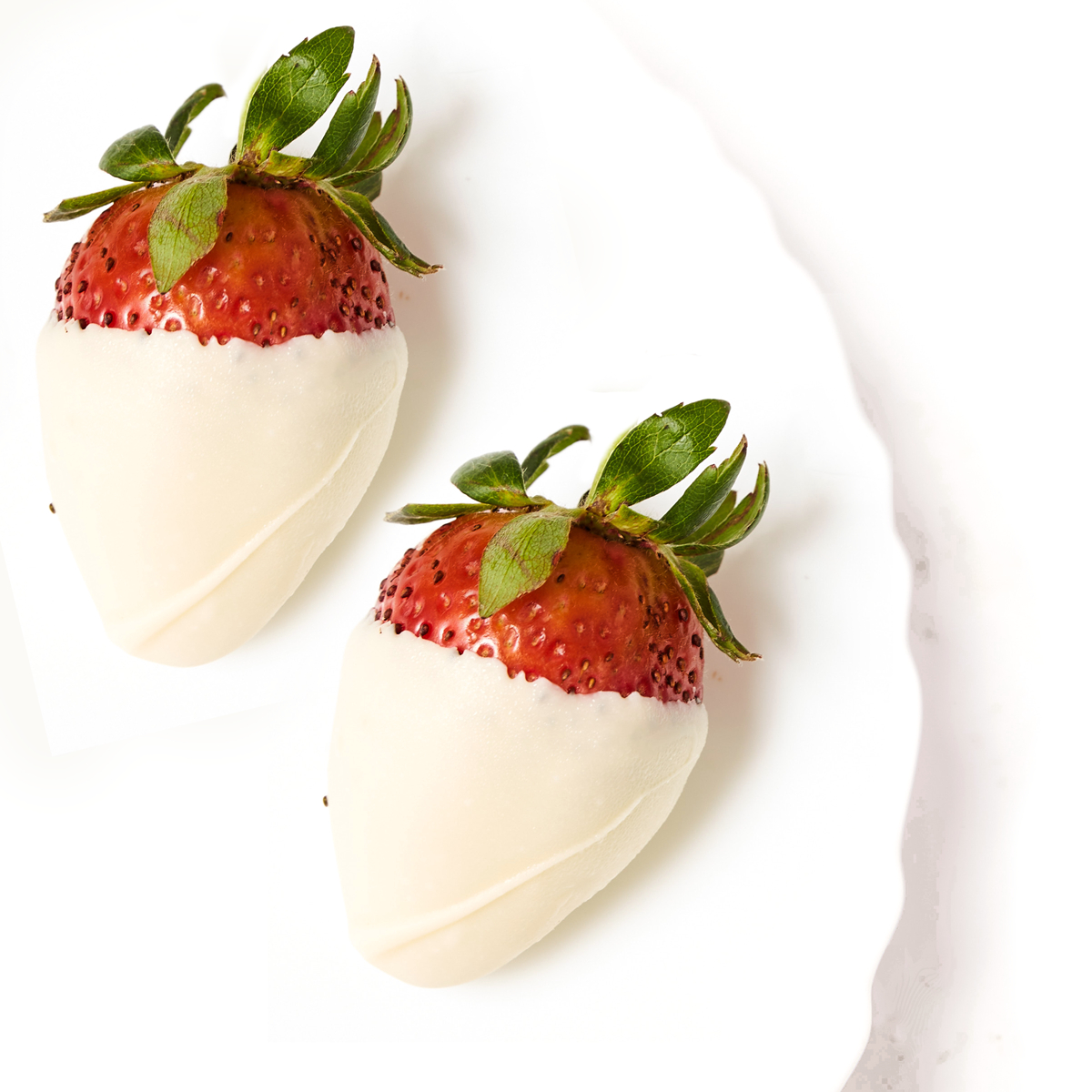 Two strawberries partially dipped in white chocolate from Godiva chocolate-covered strawberries