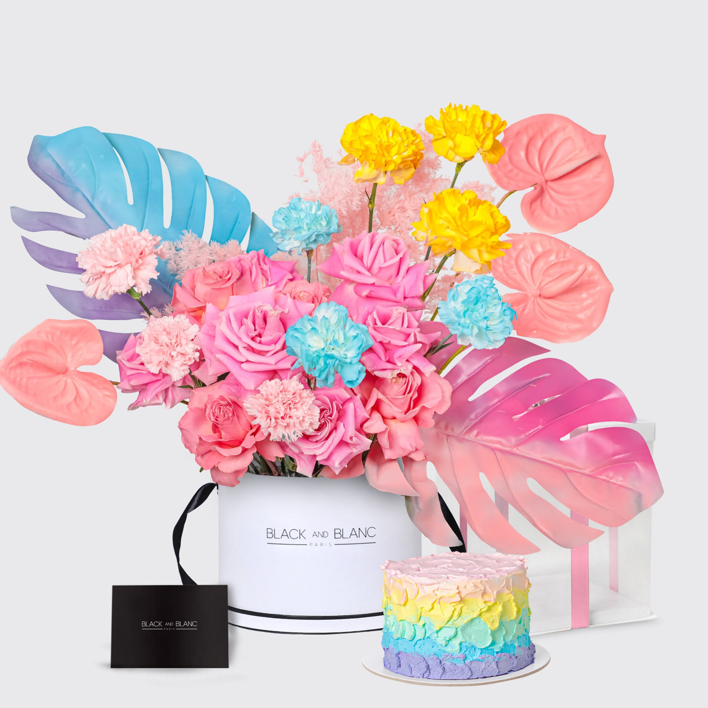 Vibrant floral arrangement in a white box with tropical leaves and a cute rainbow cake