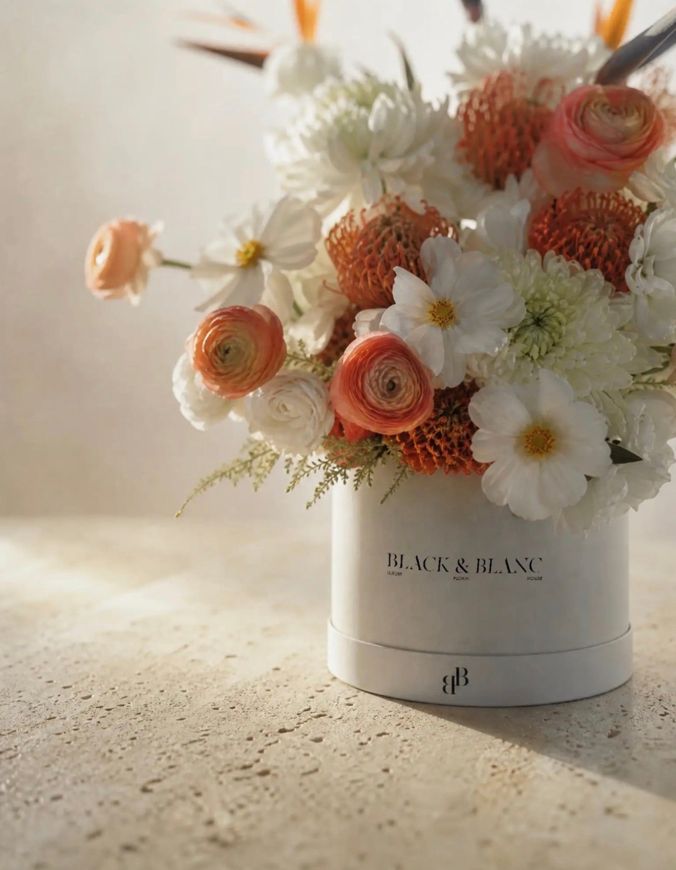 Peach ranunculus, pincushion protea and white cosmos in a Black & Blanc box in late afternoon light