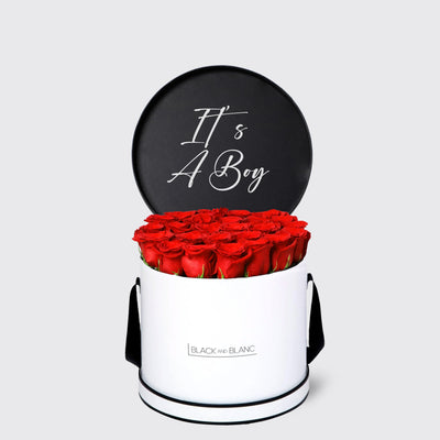 Cylindrical white box of red roses with black lid saying It’s A Boy in cursive writing