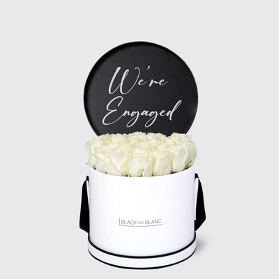 Elegant white floral arrangement in a round box with engagement announcement sign