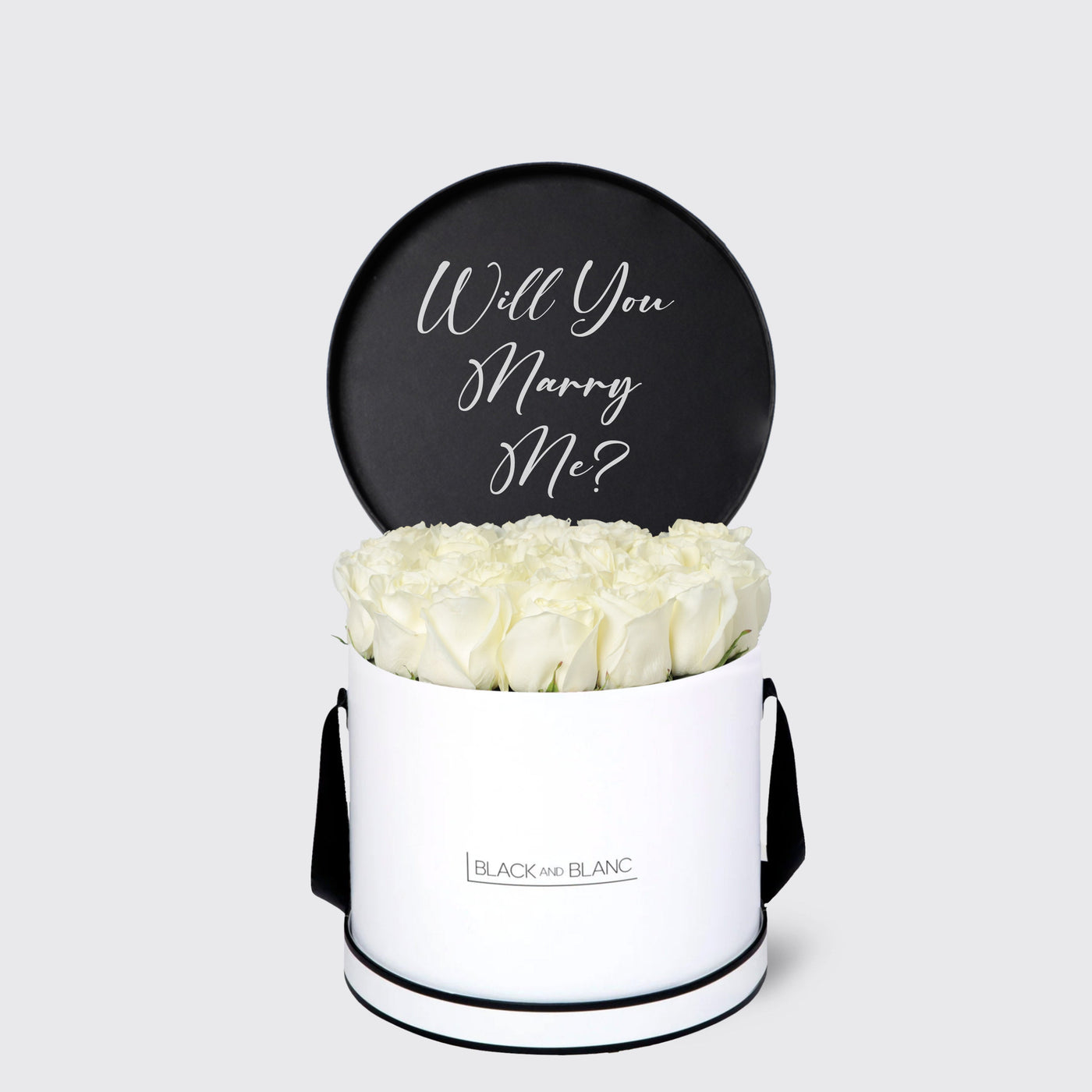 Elegant white cylindrical box of roses with a black sign saying Will You Marry Me