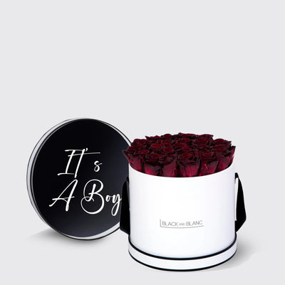 Cylindrical white box of infinity roses in red with black lid saying It’s A Boy