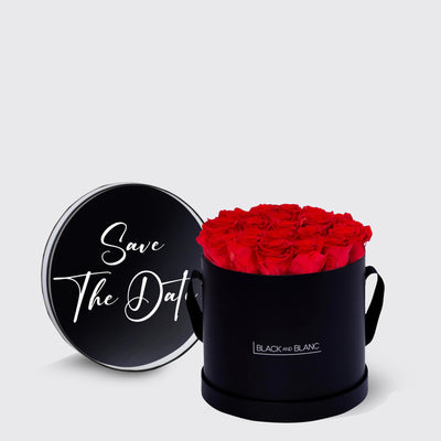 Black cylindrical box of infinity roses with red blooms and Save The Date lid