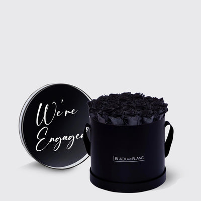 Black cylindrical box with infinity roses and a lid that says We’re Engaged