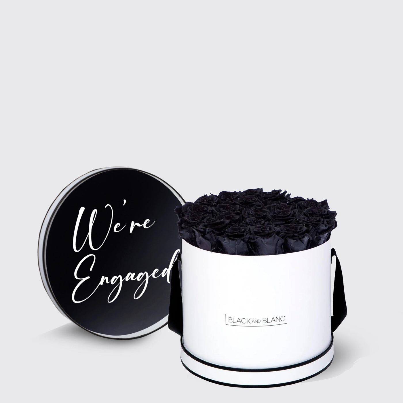 Cylindrical white box with infinity roses and black lid saying We’re Engaged in script