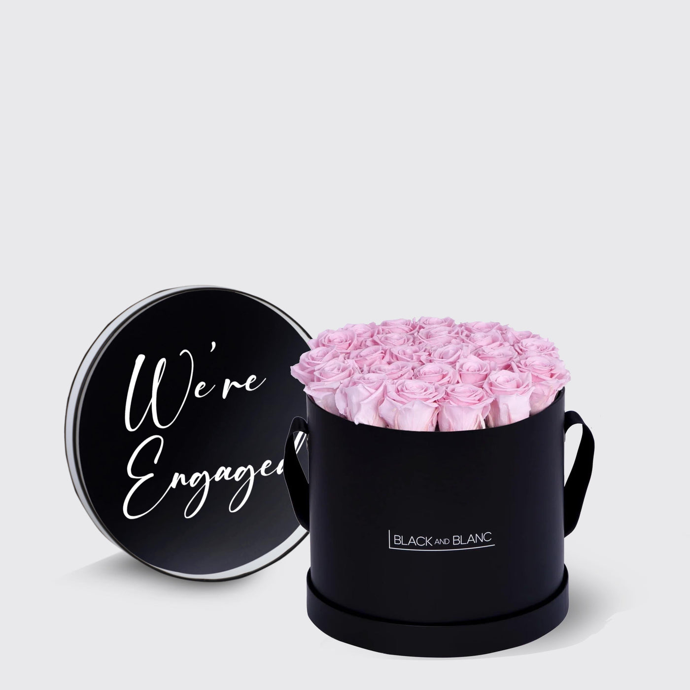 Circular black box of infinity roses with pink blooms and We’re Engaged lid script