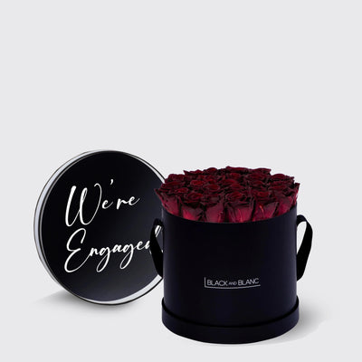 Circular black box of infinity roses with a lid saying We’re Engaged in white script