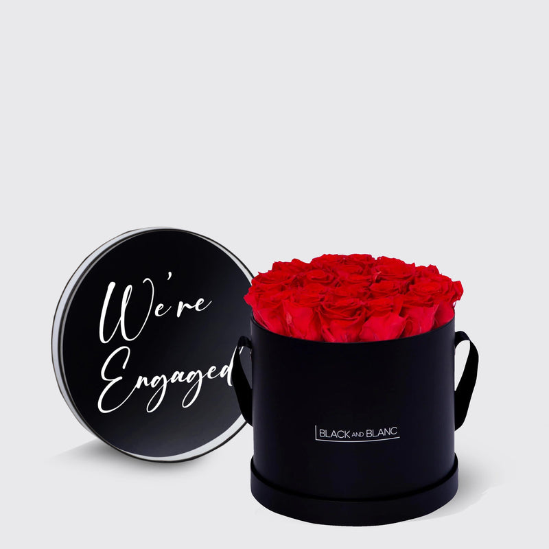 Circular black box with infinity roses and We’re Engaged lid in white script