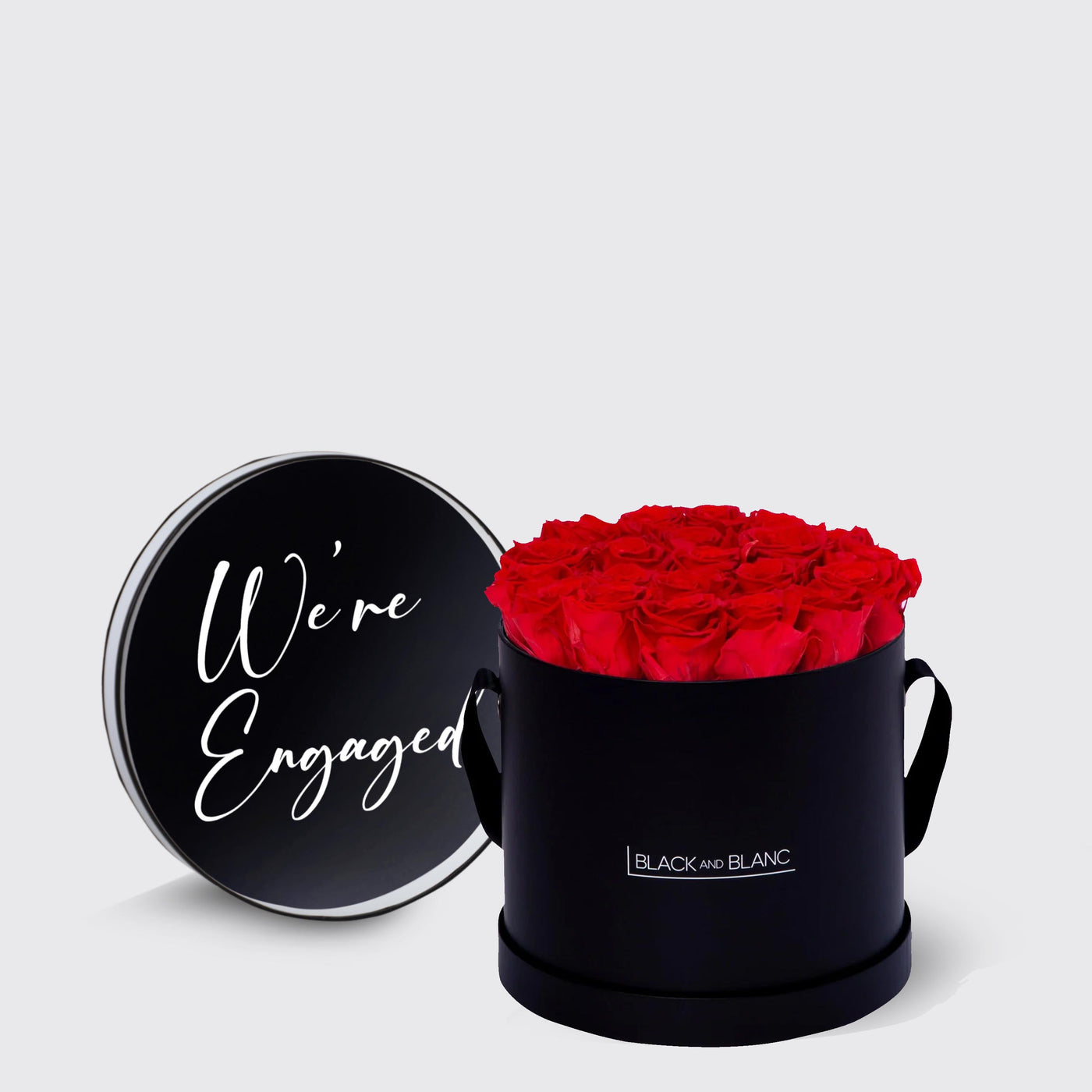 Circular black box with infinity roses and We’re Engaged lid in white script