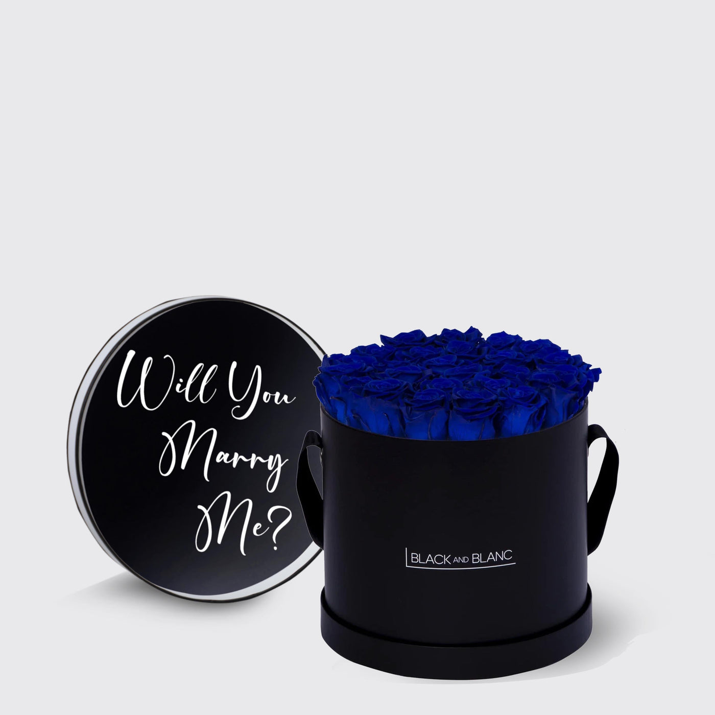 Circular black box with blue infinity roses and lid asking Will You Marry Me