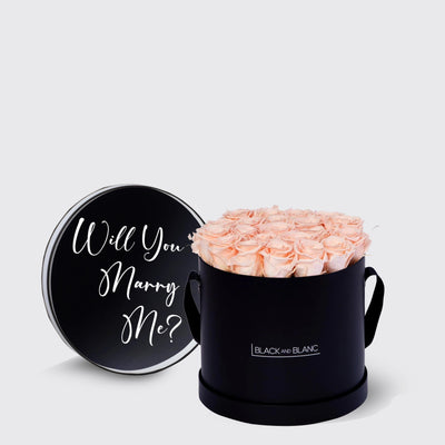 Circular black box with light pink infinity roses and a lid that says Will You Marry Me