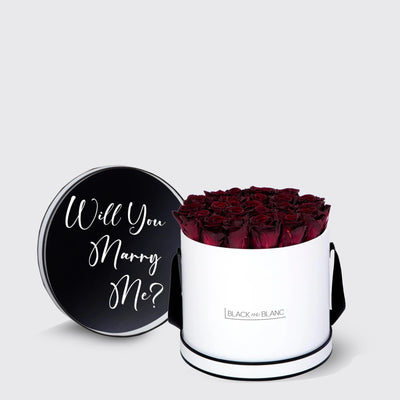 Cylindrical white box of infinity roses with black lid saying Will You Marry Me