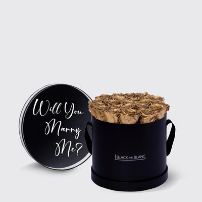 Circular black box with golden infinity roses and lid asking Will You Marry Me