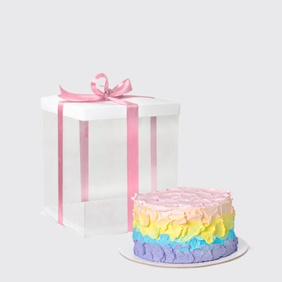 Colorful pastel-frosted Rainbow Essence Set cake next to a gift box with pink ribbon